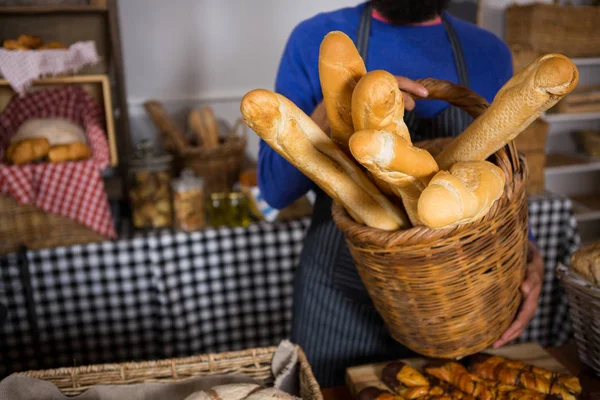 Sección media del personal sosteniendo canasta de mimbre de panes franceses en el mostrador — Foto de Stock