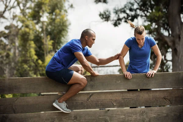 Entraîneur masculin aidant la femme à escalader un mur en bois — Photo