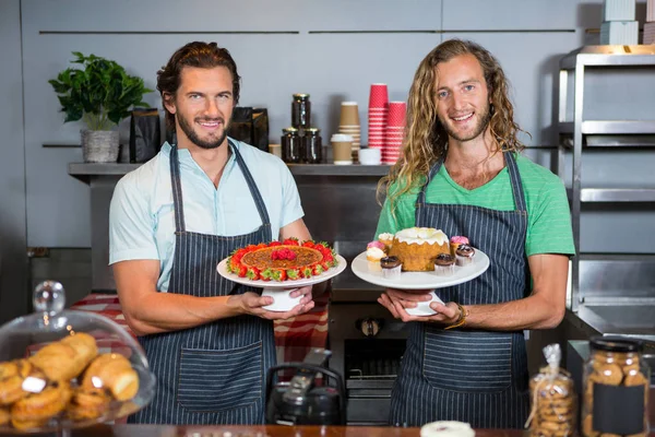 Retrato de dos bastones masculinos sosteniendo postre en el soporte de la torta en el mostrador — Foto de Stock