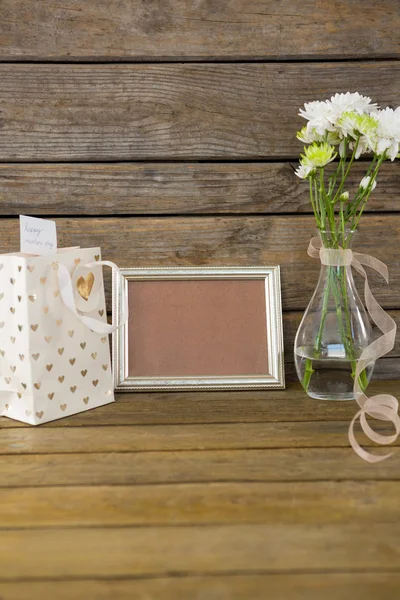 Sacchetto regalo, cornice e vaso di fiori su superficie di legno — Foto Stock