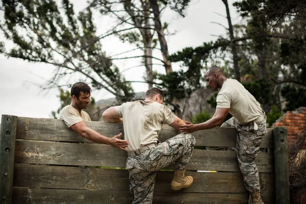 나무 벽을 등반 하는 사람을 돕는 군인 — 스톡 사진