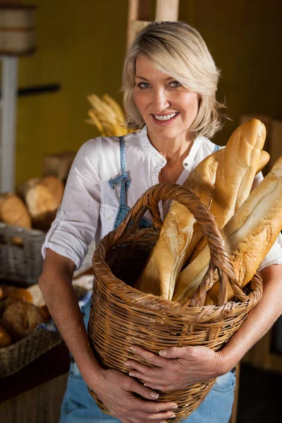 Female staff holding basket of baguettes in bakery section — Stock Photo, Image