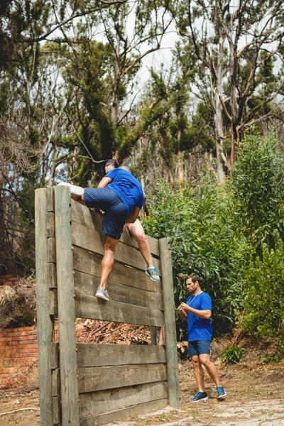 Trainerin hilft Mann beim Klettern einer Holzwand — Stockfoto