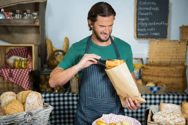 Glimlachende man personeel brood verpakken in papieren zak — Stockfoto