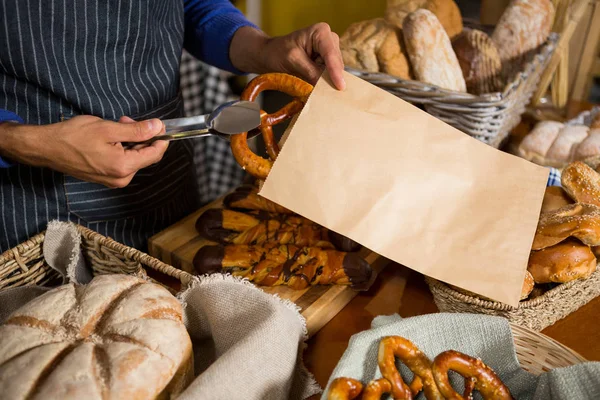 Mid sectie vanpersoneel krakeling brood verpakken in papieren zak aan balie — Stockfoto