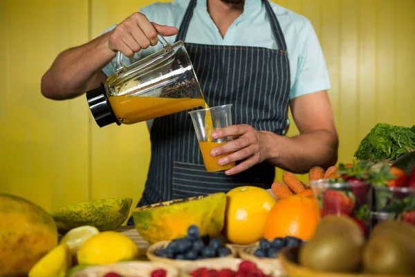 Male staff pouring juice into glass at counter — Stock Photo, Image