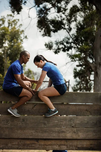 Entraîneur masculin aidant la femme à escalader un mur en bois — Photo