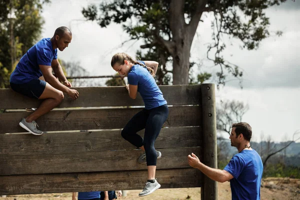 Pelatih laki-laki membantu wanita memanjat dinding kayu — Stok Foto