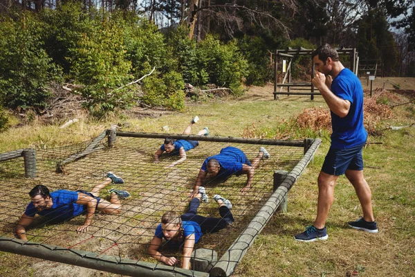 Tilpassede personer som kryper under nettet under hinderløypen – stockfoto