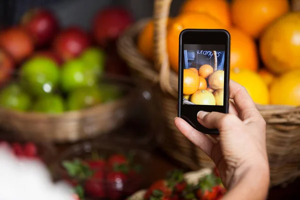Cliente fêmea tirando fotos de laranjas no celular na seção orgânica — Fotografia de Stock