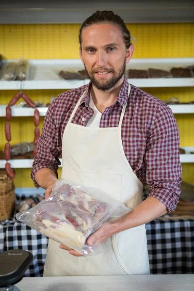 Ritratto di uomo sorridente che tiene un pacchetto di carne al bancone — Foto Stock