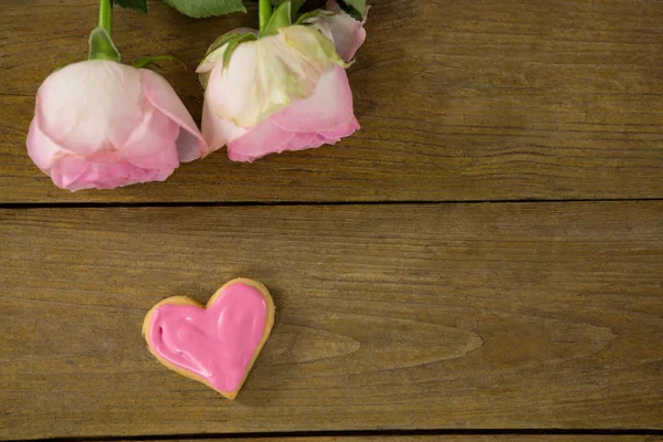 Rosas cor-de-rosa com biscoitos em forma de coração na prancha de madeira — Fotografia de Stock