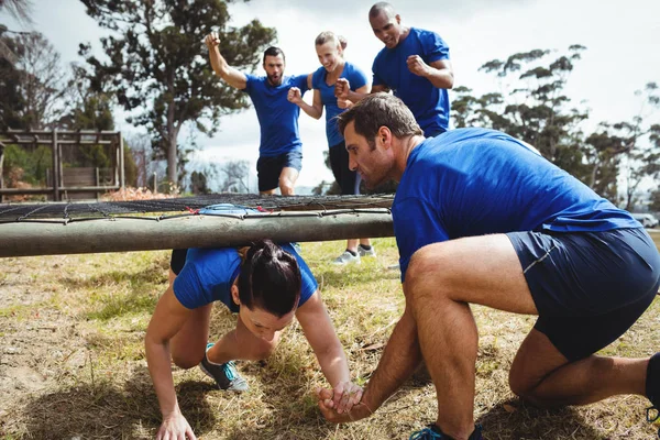 Fit mulher rastejando sob a rede durante o curso de obstáculo, enquanto as pessoas aptas torcendo — Fotografia de Stock