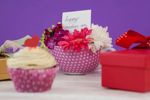 Cup cake, doos van de gift en verse bloemen op houten oppervlak — Stockfoto