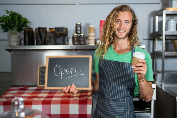 Pessoal masculino segurando uma placa com sinal aberto e copo de café descartável — Fotografia de Stock