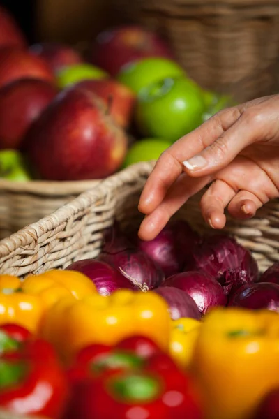 Hand of female costumer selecting vegetables from wicker basket — Stock Photo, Image