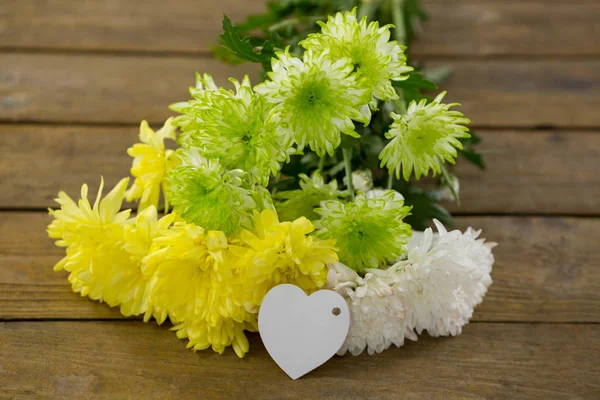 Ramo de flores amarillas con etiqueta de forma de corazón en tablón de madera — Foto de Stock