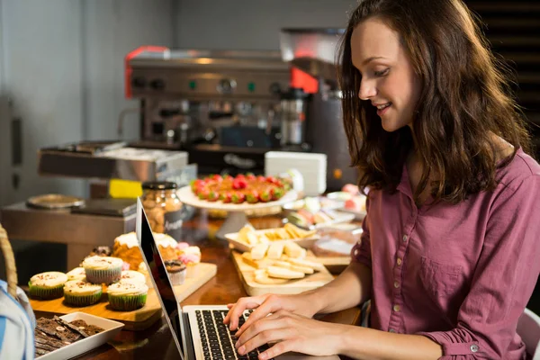 Frau benutzt Laptop an Bäckereitheke — Stockfoto