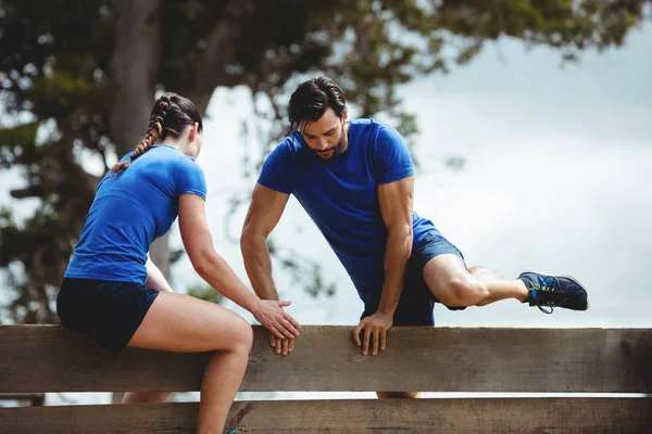 Entraîneur féminin aidant l'homme à escalader un mur en bois — Photo