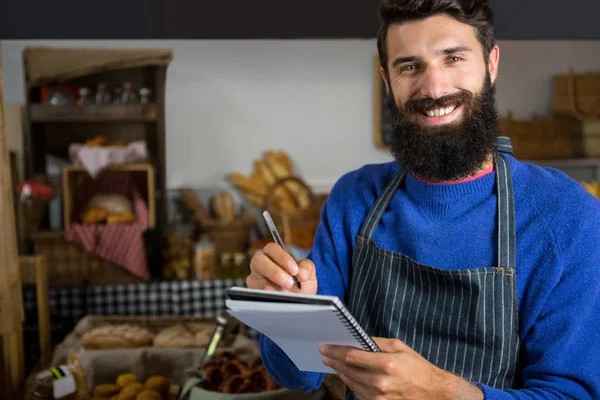 Sorrindo pessoal masculino escrevendo no bloco de notas no balcão na padaria — Fotografia de Stock
