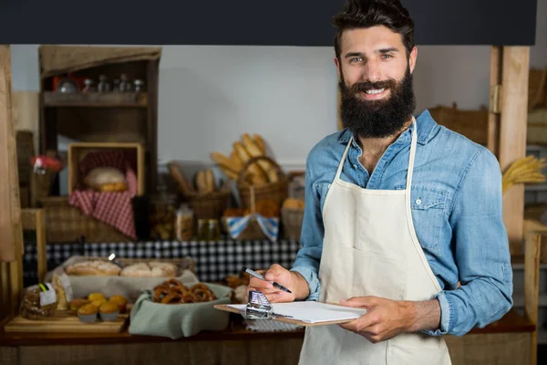 Salesman writing on clipboard at counter in grocery shop — Stock Photo, Image