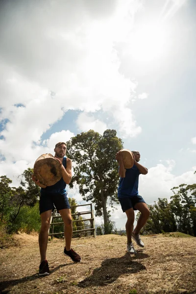 Ajuste los hombres levantando troncos de madera pesados durante la carrera de obstáculos — Foto de Stock