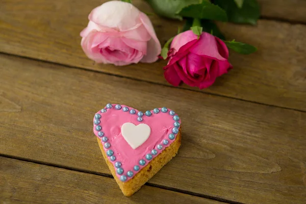 Ahşap tahta üzerinde kalp şekli kurabiyeyle pembe güller — Stok fotoğraf
