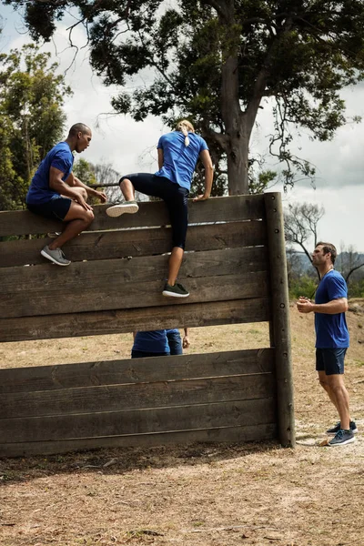 Männlicher Trainer hilft Frau eine Holzwand zu erklimmen — Stockfoto