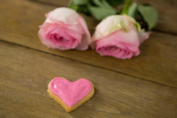 Ahşap tahta üzerinde kalp şekli kurabiyeyle pembe güller — Stok fotoğraf
