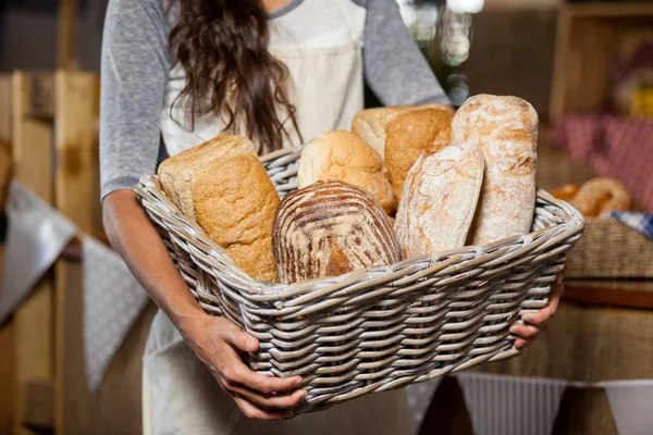 Vrouwelijk personeel houden rieten mand van verschillende broden op de teller in bakkerij winkel — Stockfoto