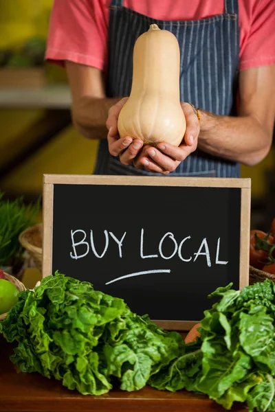 Mid section of male staff holding butternut squash with slate board in organic section — Stock Photo, Image