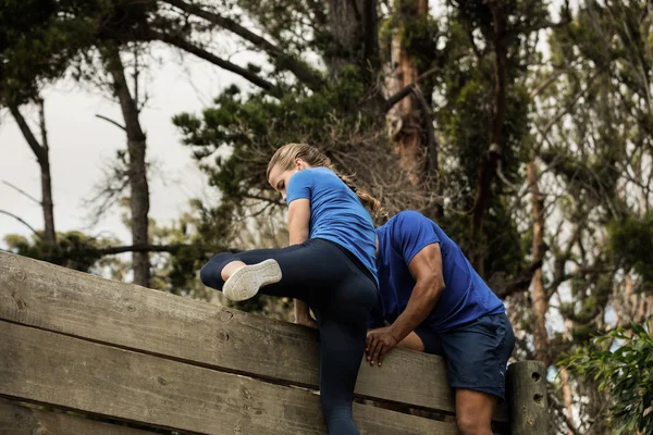 男性トレーナーの木製の壁を登るには女性を支援 — ストック写真