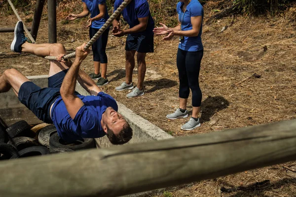 Hombre cruzando la cuerda durante la carrera de obstáculos mientras la gente lo anima —  Fotos de Stock