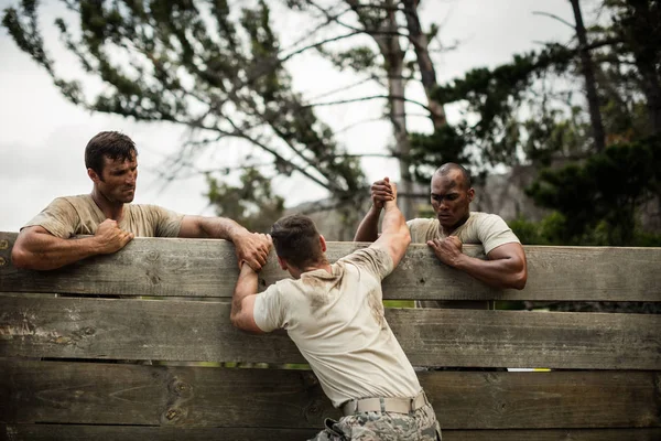 Soldados ayudando al hombre a escalar la pared de madera — Foto de Stock