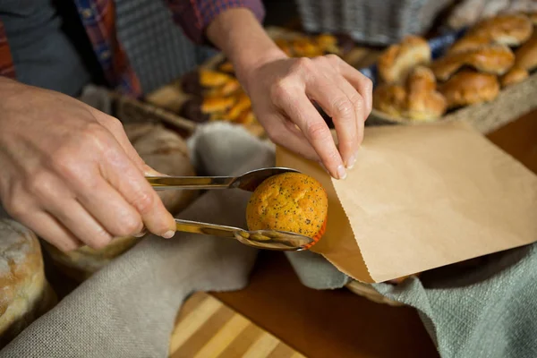 Mid section of staff packing cup cake in paper bag at counter — Stock Photo, Image