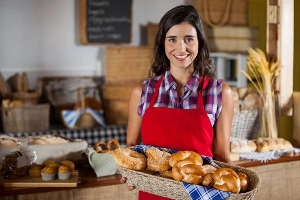 Bastone femminile sorridente che tiene cesto di vimini di vari pani al bancone — Foto Stock