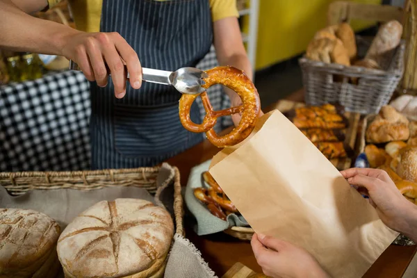 Seção média do pessoal de embalagem de pão pretzel em saco de papel no balcão — Fotografia de Stock