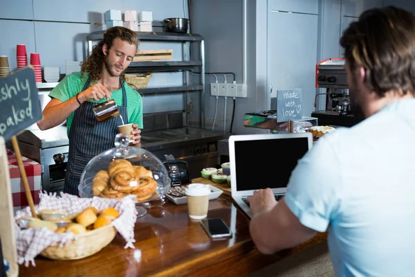 Kunden använder laptop vid disken medan personalen förbereda kaffe — Stockfoto