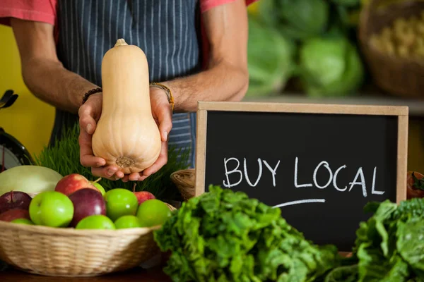 Mid section of male staff holding butternut squash with slate board in organic section — Stock Photo, Image