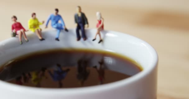 坐在咖啡杯子的边缘上的微型商务人士 — 图库视频影像