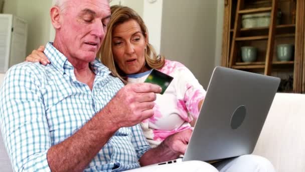 Sonriendo pareja de ancianos haciendo compras en línea en el ordenador portátil en la sala de estar — Vídeo de stock
