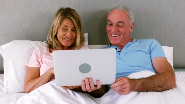 Smiling couple lying on bed and using laptop — Stock Video