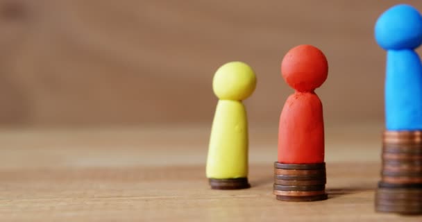 Grupp av röda, blå och gula figurer som står på pålar av mynt — Stockvideo