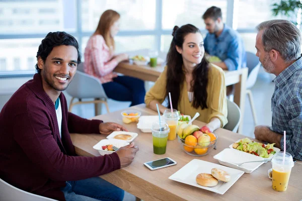 Uomo sorridente che mangia con i suoi colleghi — Foto Stock