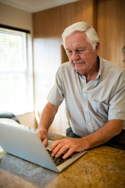 Uomo anziano utilizzando il computer portatile in cucina — Foto Stock