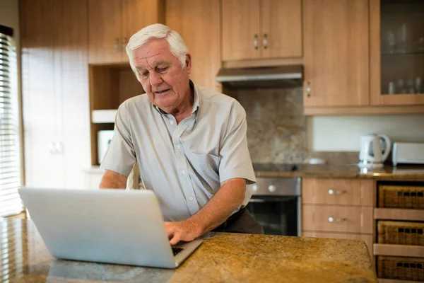 Uomo anziano utilizzando il computer portatile in cucina — Foto Stock
