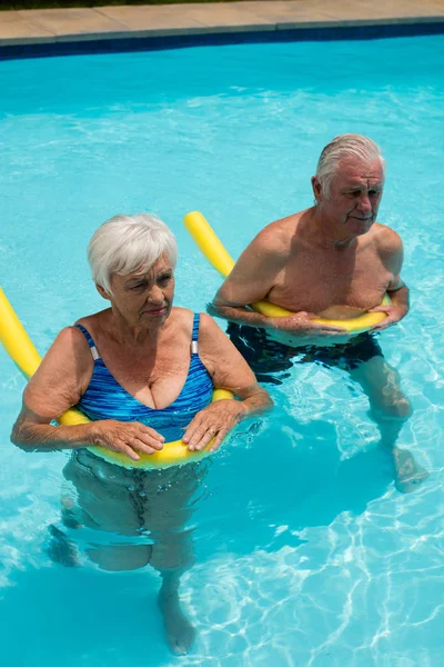 Seniorenpaar schwimmt im Pool mit aufblasbaren Schläuchen — Stockfoto