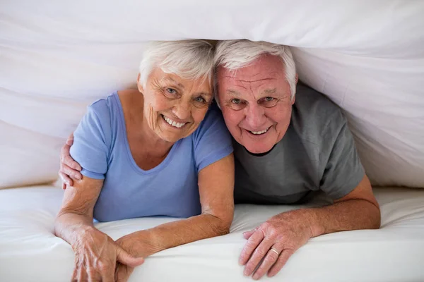 Retrato de feliz pareja de ancianos bajo la manta en la cama —  Fotos de Stock