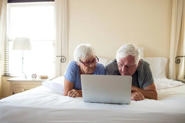 Senior couple using laptop on bed in bedroom — Stock Photo, Image