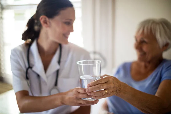 Médica feminina servindo um copo de água para a mulher idosa no quarto — Fotografia de Stock